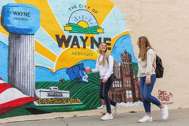 Two female students walk by a Wayne mural