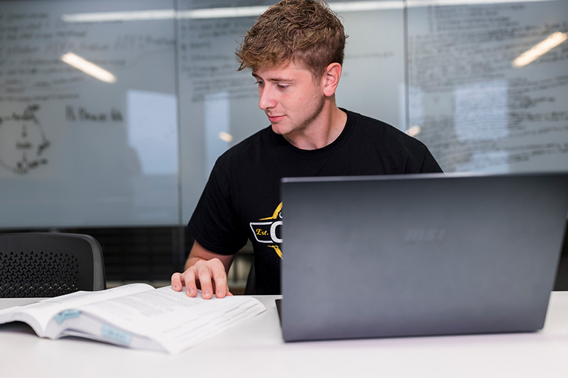 Male student studying with a book and a laptop computer