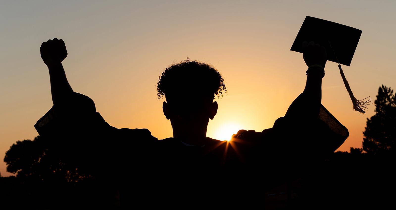 A WSC student poses with cap and gown at sunset