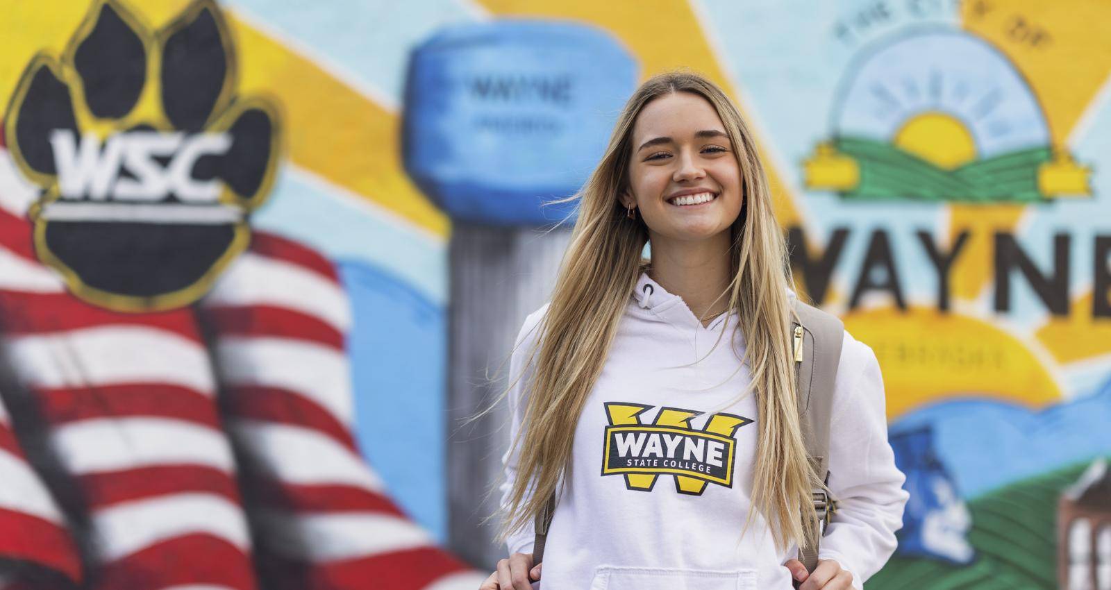 A WSC student poses in front of a Wayne mural