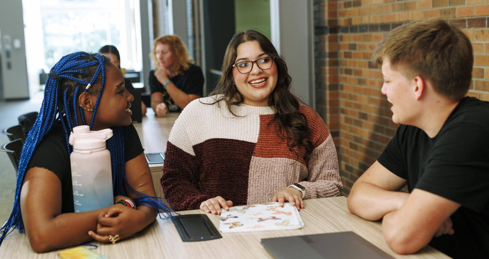 Three college students talking and smiling together at a table on campus
