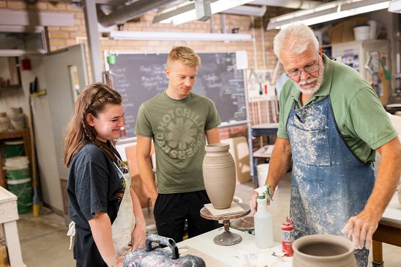 Art education degree students work with a professor in the pottery studio