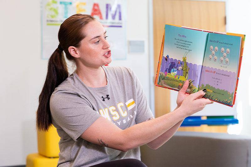 A student reads a book to a class