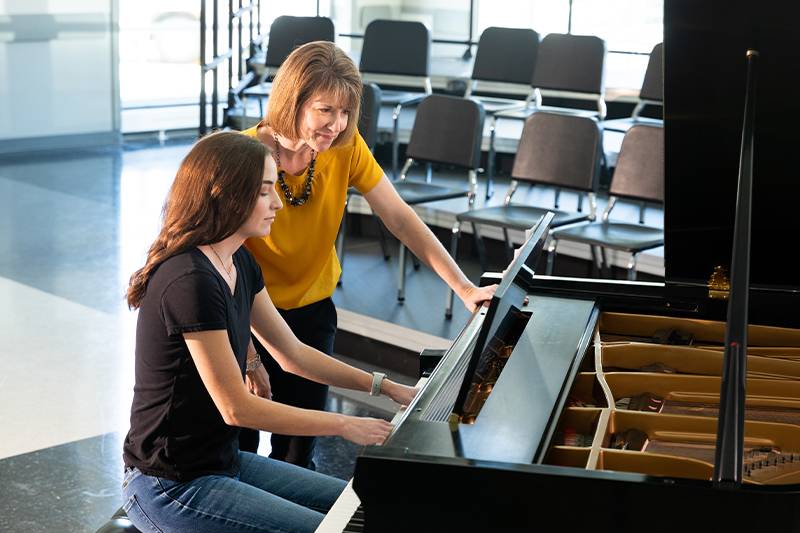 A music education degree student works on piano lessons with a music professor