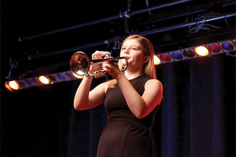 A music performance degree student plays the trumpet in a recital on stage at WSC
