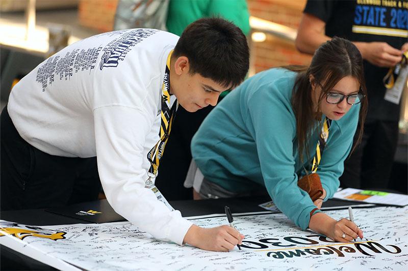 Two students sign the Class of 2030 poster at NSR