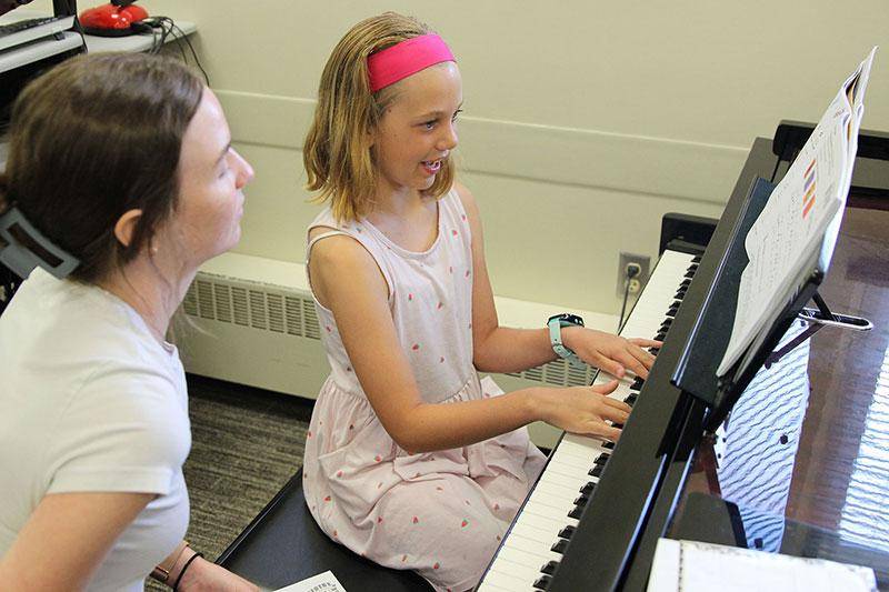 Photo of a piano student playing the piano for her teacher